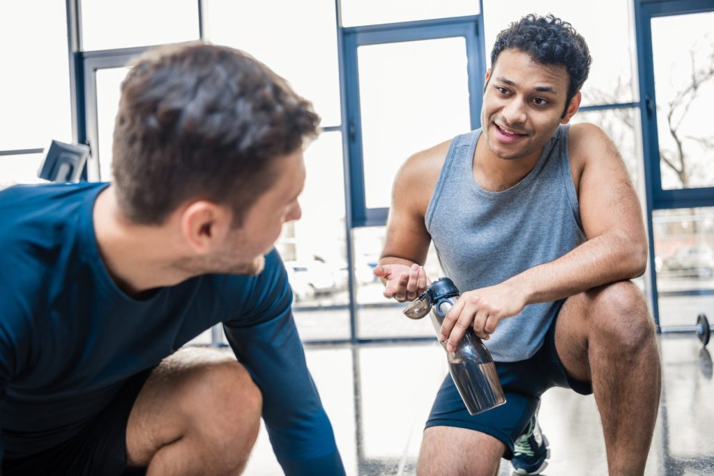 Handsome young man with bottle of water talking to friend